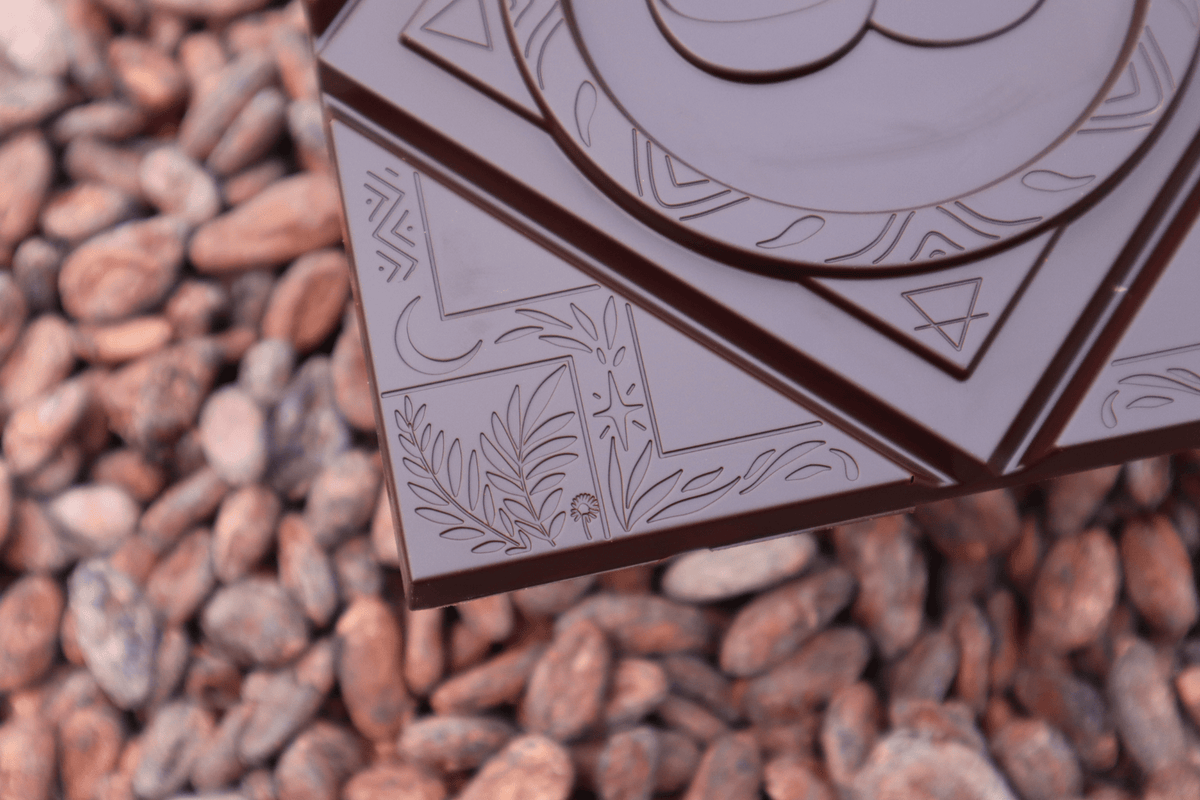 Tableta de chocolate MOOJO con motivo en relieve sobre un lecho de granos de cacao
