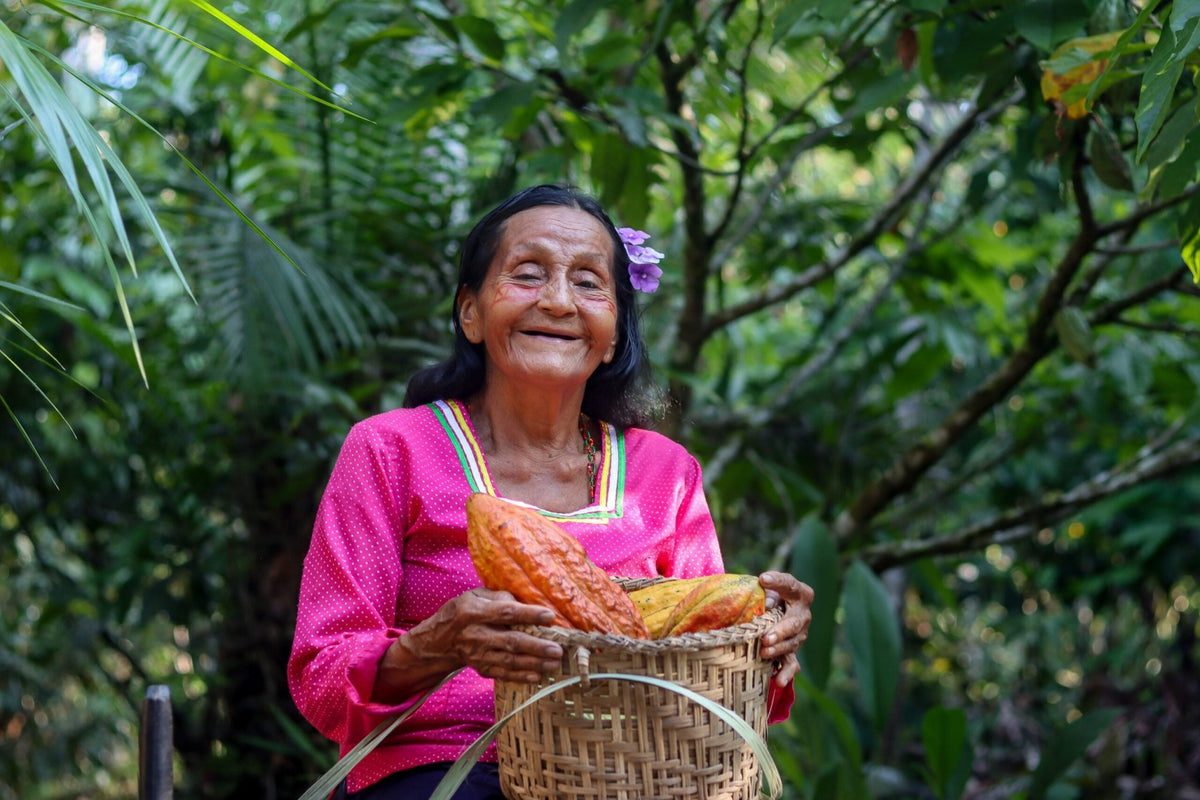 Femme souriante portant un panier de récolte dans la cacaoyère · Équateur Nacional Kallari