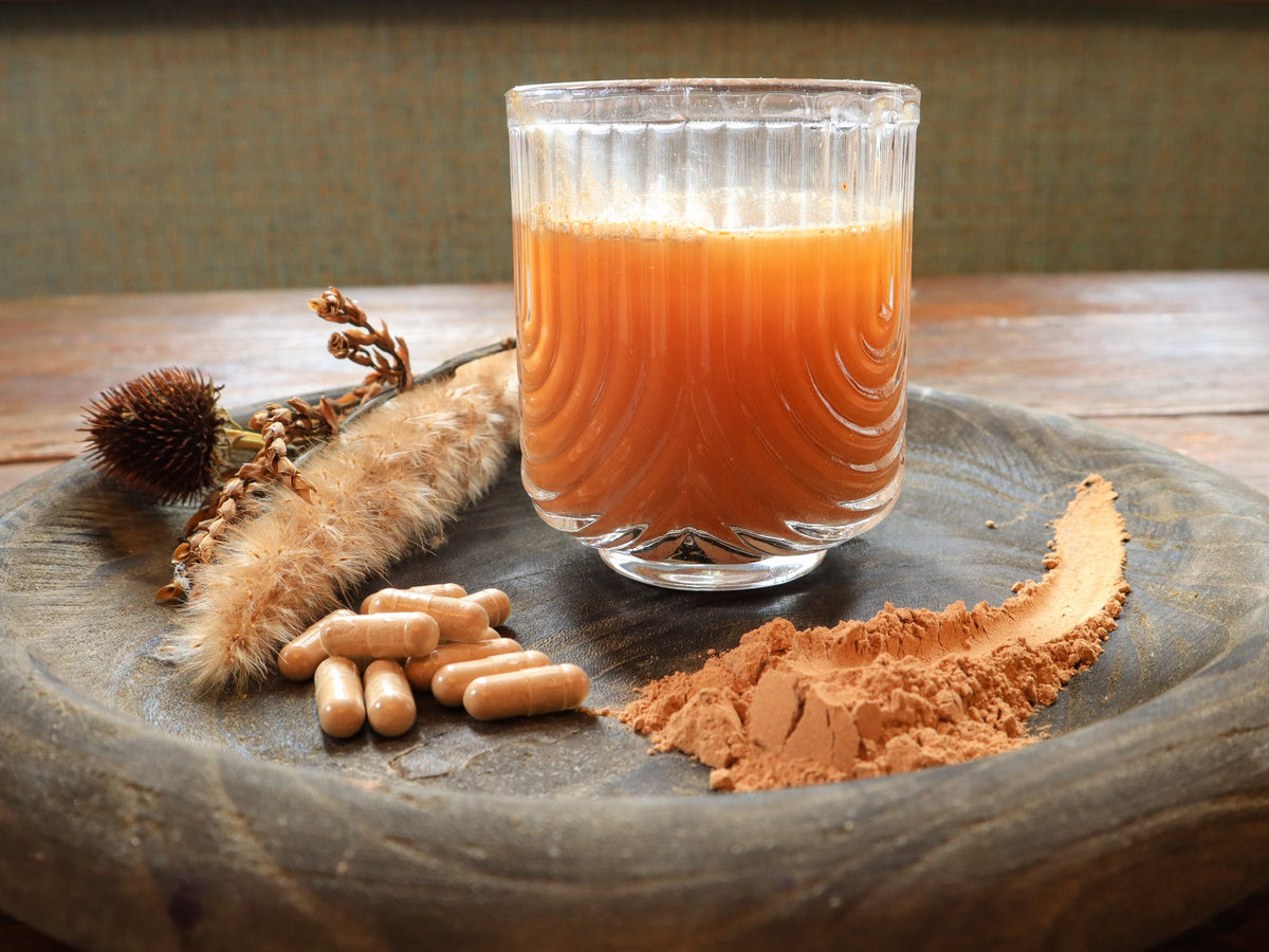 Verre de jus, poudre et gélules de camu camu sur un plateau en bois