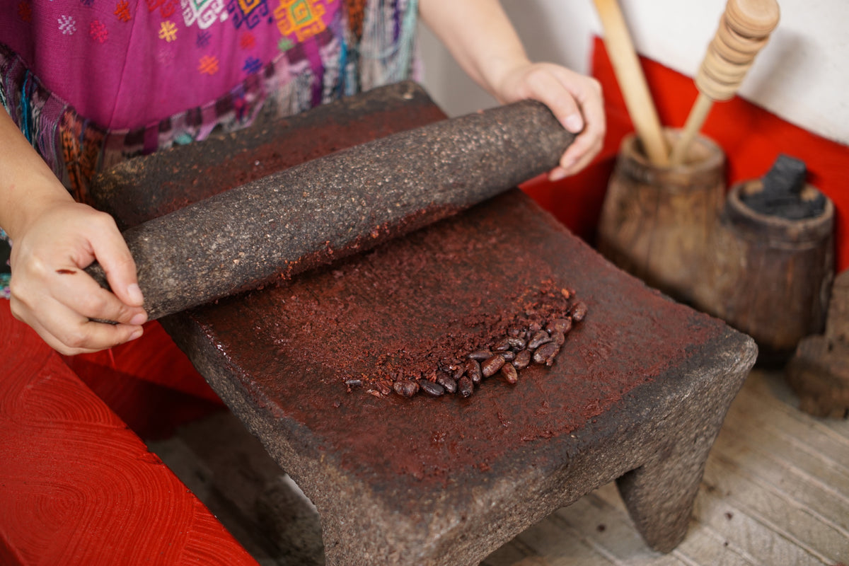 Molienda del cacao a mano sobre un metate de piedra, la pasta marrón rojiza bajo el rodillo
