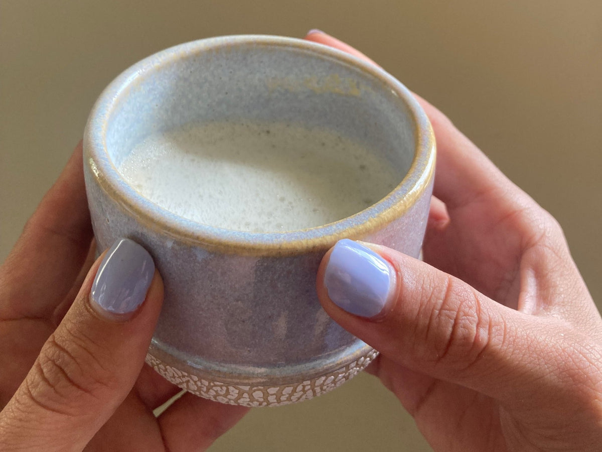 Tasse Nisha à l'émail lavande tenue à deux mains, boisson chaude mousseuse